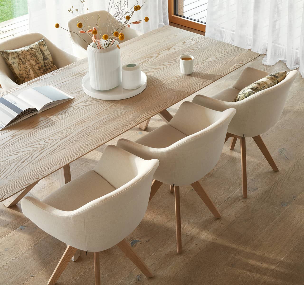 Stilvolle Esszimmerstühle mit hellem Stoffbezug und Holzbeinen an einem großen Esstisch.